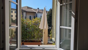 A view through a window with a white frame, revealing a balcony with potted plants and an umbrella. - Charming retreat with terrace over Pisa's hidden gardens (Pisa)
