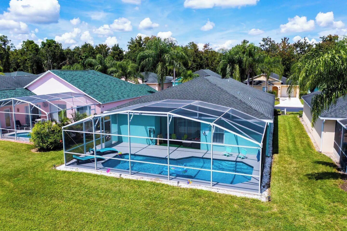 Una piscina techada con cerramiento de vidrio, rodeada por un césped cuidado y casas vecinas.