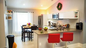 A modern kitchen with a central island, bar stools, a dining area with a table and chairs, and a refrigerator. -     Family Pool Home-Near Disney, Food Festivals & Events- Book Now (Davenport)