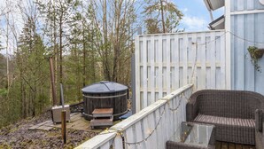 Une terrasse en bois avec un jacuzzi, des meubles en osier et une clôture blanche.
