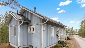 Une petite maison en bois d’un seul étage, avec un toit en pente, une véranda et une allée en terre.