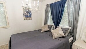 Une chambre à coucher avec un lit, des oreillers, une commode, un lustre et des rideaux.