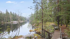 A forested area with a wooden boardwalk leading to a lake. - Korpilammenhuvilat 7a by Interhome (Espoo)