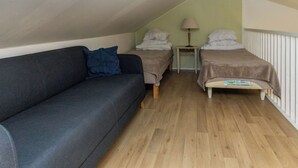 A small, cozy room with a dark gray sofa, two single beds, a small table with a lamp, and a radiator. - Korpilammenhuvilat 7a by Interhome (Espoo)