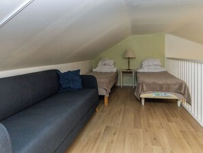 Ein kleiner, gemütlicher Raum mit einem dunkelgrauen Sofa, zwei Einzelbetten, einem Tisch mit einer Lampe und einem Heizkörper.