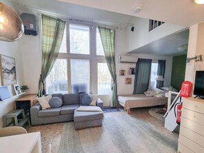 Ein gemütlicher Wohnraum mit Sofa, Bett, Schreibtisch und einer Wendeltreppe.