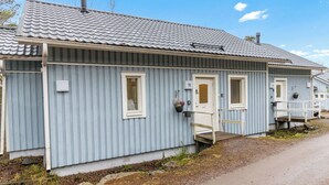 A row of blue wooden cabins with a tiled roof, each with a small porch and a door marked with a number.