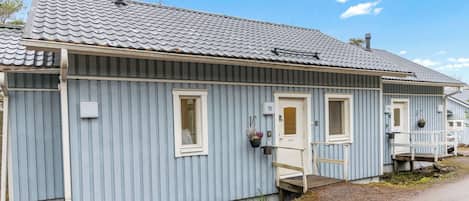 Une rangée de cabanes en bois bleues, coiffées d’un toit de tuiles, chacune dotée d’un petit porche et d’une porte portant un numéro.
