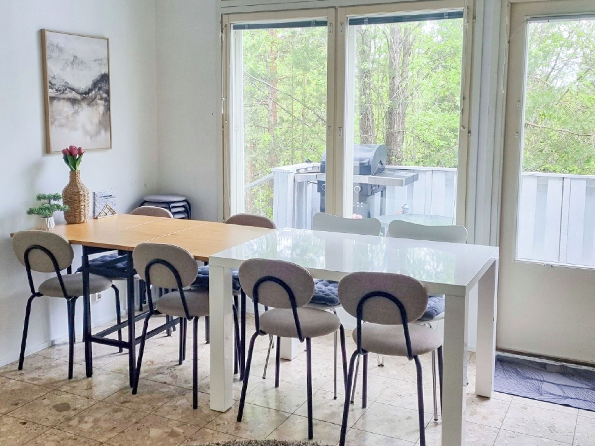 A dining area with a white table and chairs, a vase with flowers, and a painting on the wall.