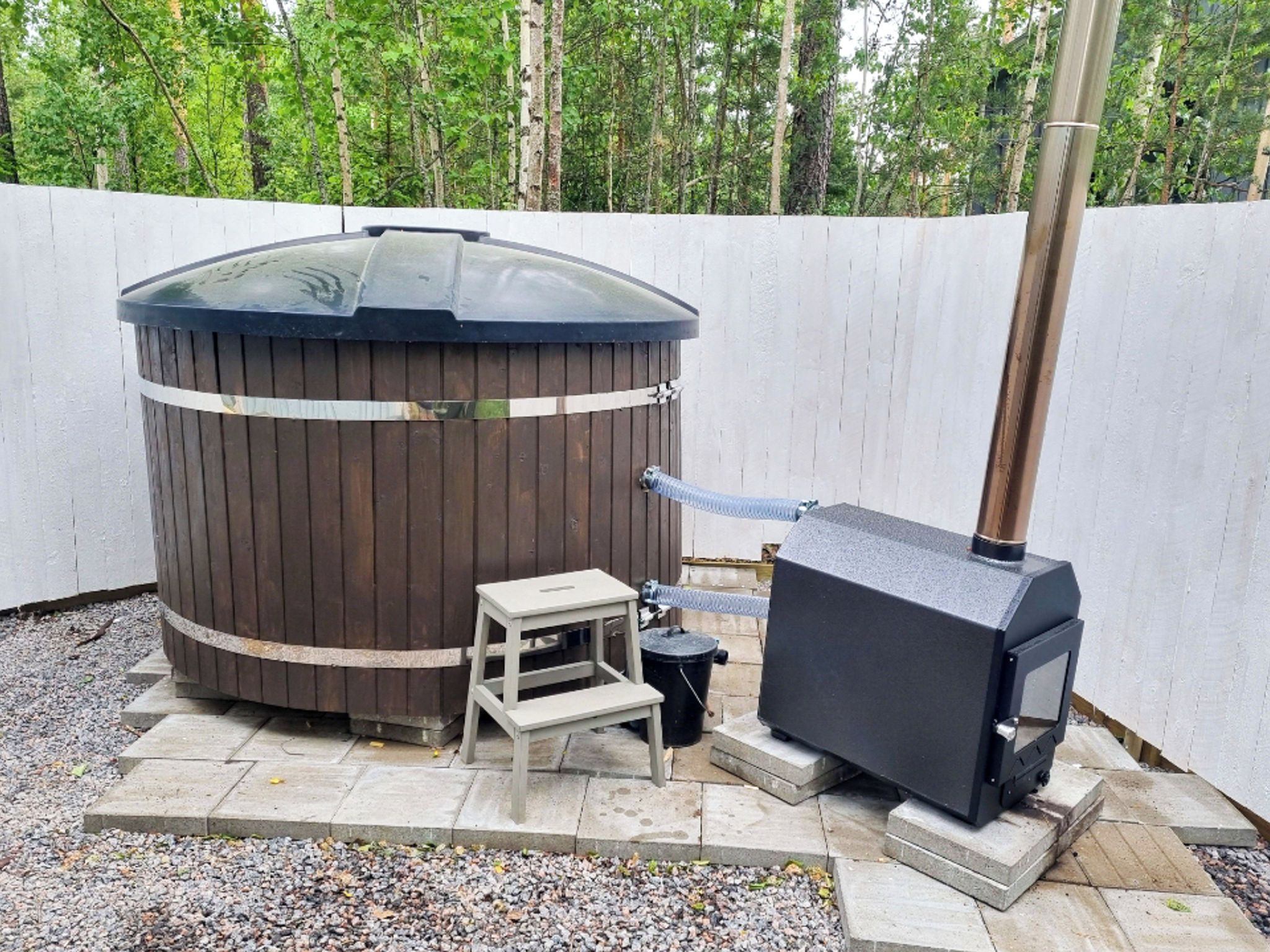 Sauna, jonka ulkoseinät ovat puuta, siinä on savupiippu sekä lähellä pieni pöytä ja jakkara.