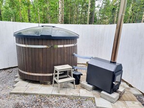 Un sauna avec une structure extérieure en bois, une cheminée, ainsi qu’une petite table et un tabouret à proximité.