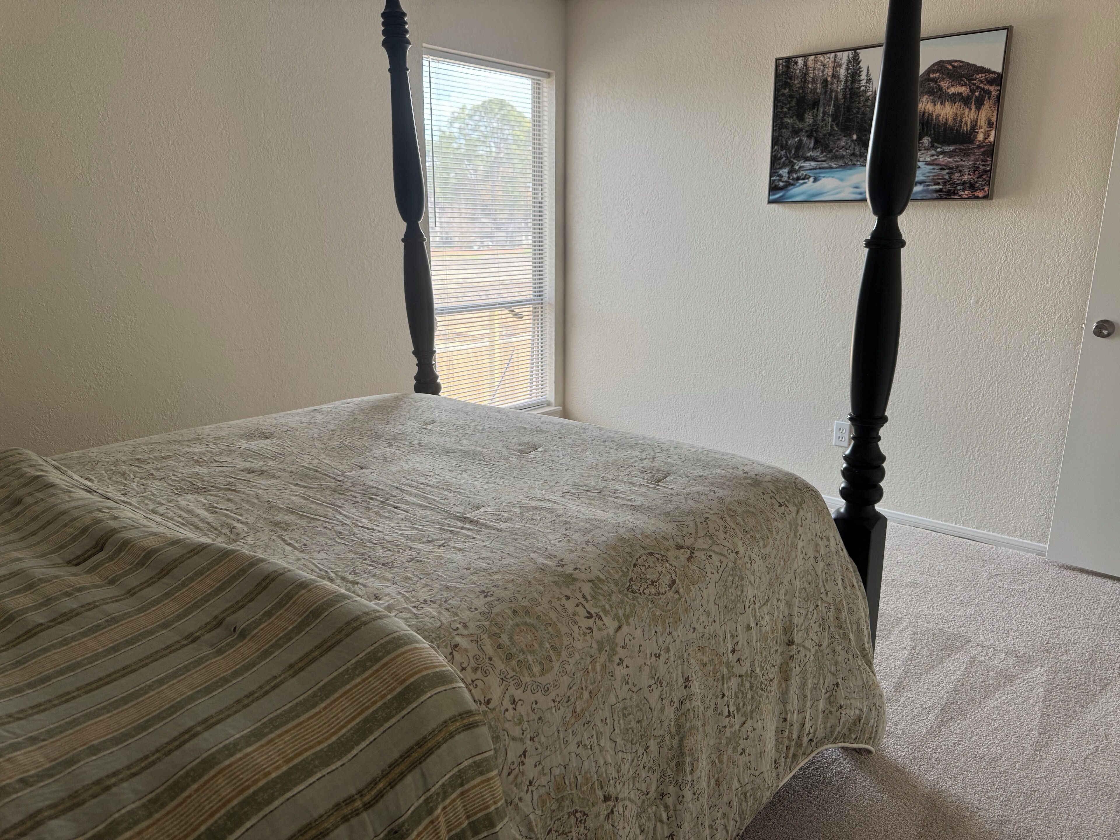 Un dormitorio con una cama con dosel, una ventana con persianas y un cuadro en la pared.