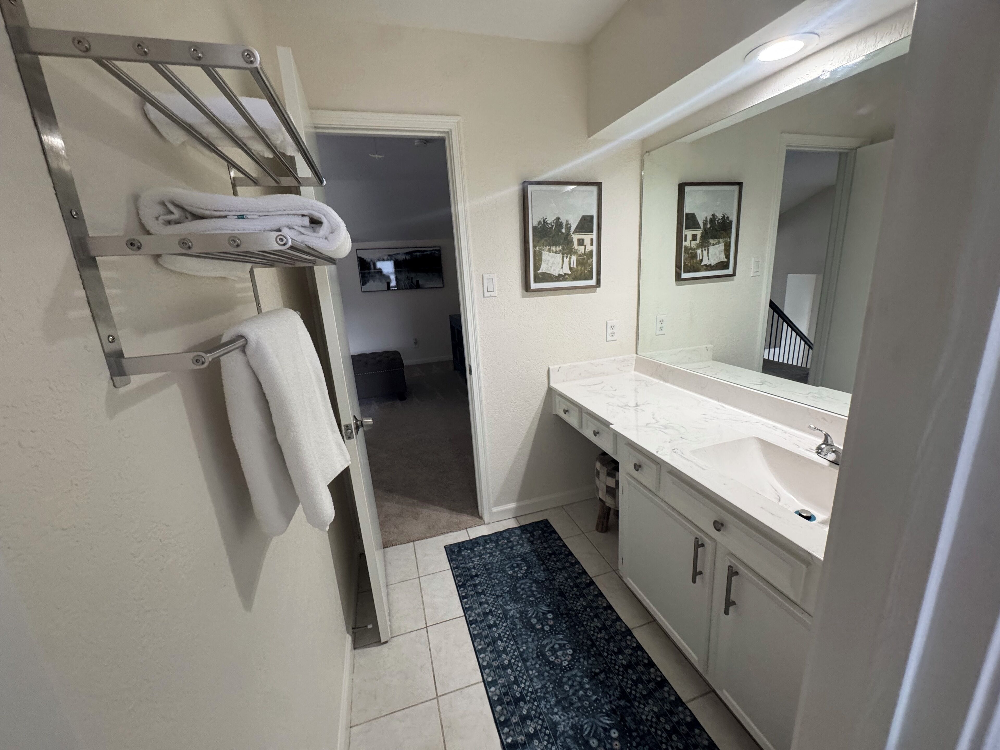 Un baño con lavamanos blanco, un espejo grande y un perchero para toallas.