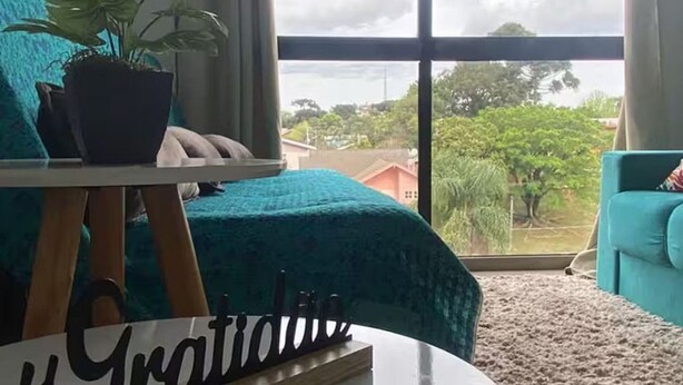 Una habitación con una cama, una planta en maceta, una mesa redonda y vistas al exterior a través de amplios ventanales.