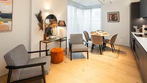 Un soggiorno moderno con zona pranzo, che include un divano, poltrone, un tavolino da caffè e un piccolo poggiapiedi arancione.