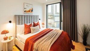 Una camera da letto moderna con un letto grande, una testiera grigia imbottita e vista sulla città attraverso un'ampia finestra.