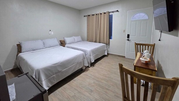 Ett hotellrum med två sängar, en trästol, ett bord med en kopp och en korg samt en tv som är monterad på väggen.