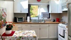 Ett kompakt kök med vita skåp, en mikrovågsugn, en spis och ett fönster med gardiner.