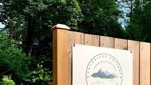 En träport med en skylt som lyder: ”Snugglers Cottage, Bowen Island, BC, 604.562.0251”.