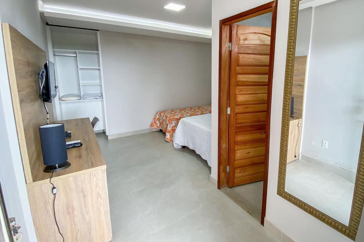 A bedroom with a wooden door, a bed with a floral bedspread, a bedside table with a lamp, and a wardrobe with a mirror.