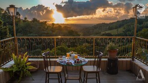 A terrace with a table set for dining, overlooking a scenic landscape with hills and a sunset. - Pousada Recanto Sol Nascente (Rio Formoso)