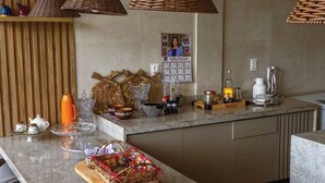A modern kitchen with a central island, hanging wicker pendant lights, and a variety of kitchenware and decorations. - Pousada Recanto Sol Nascente (Rio Formoso)
