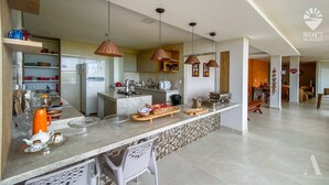 A modern kitchen with a central island, hanging pendant lights, and a dining area with a bench. - Pousada Recanto Sol Nascente (Rio Formoso)