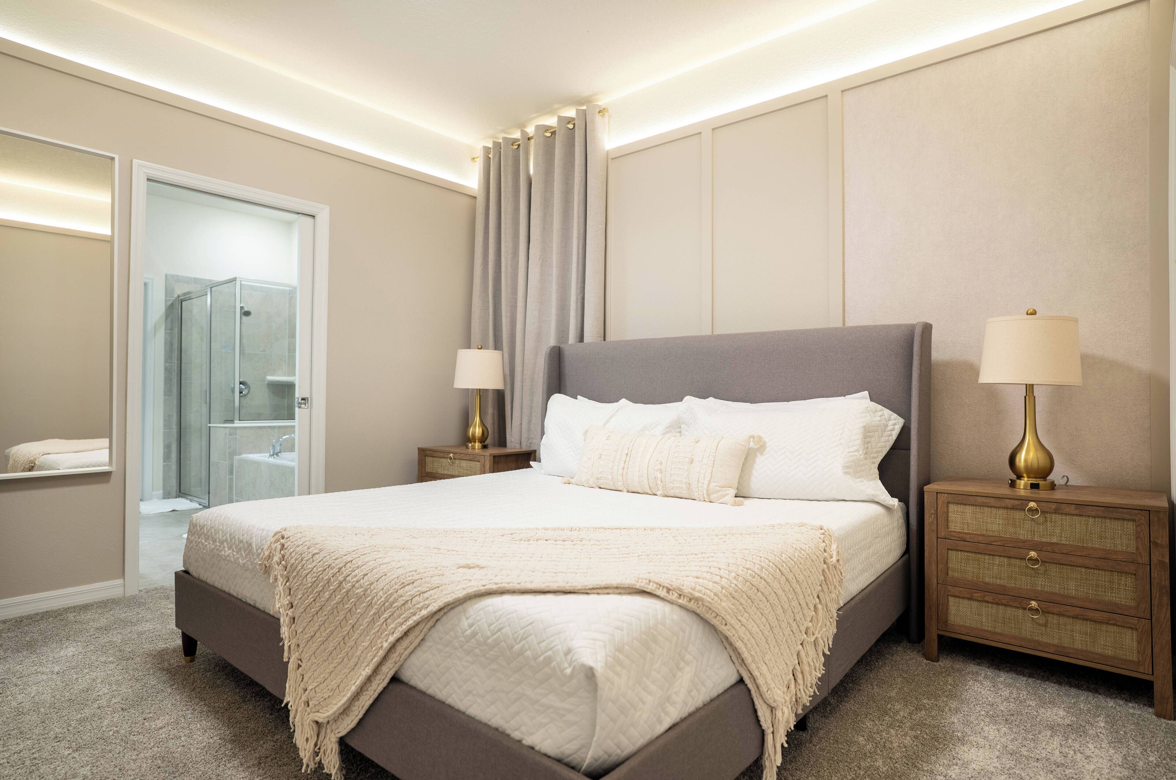 Ein Schlafzimmer mit einem großen Bett, zwei Nachttischen mit Lampen, einem zusätzlichen Tisch mit Lampe, einer Duschkabine aus Glas und einer Tür zu einem Badezimmer.