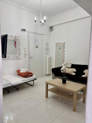 Ein sauberes, modernes Zimmer mit einem Bett, einer Couch, einem kleinen Tisch und einem Spiegel mit aufwendigen Rahmen.