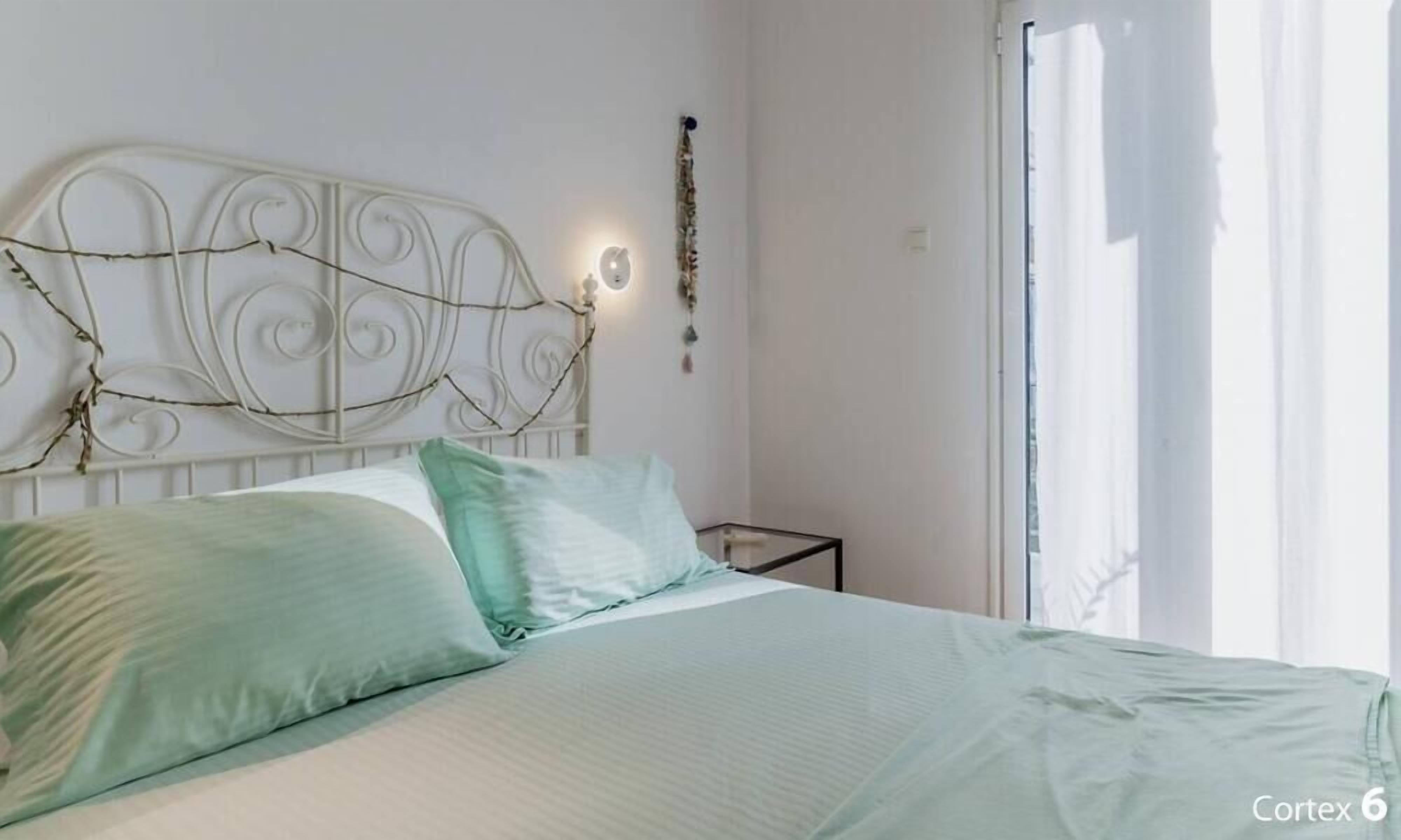 A bedroom with a white headboard, two pillows, a bedside table, and a window with curtains.