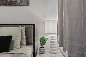 Un lit bien fait, avec des oreillers, une petite plante en pot, une lampe blanche et une table de chevet en marbre.