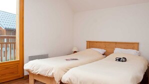 Una habitación con dos camas de madera, una ventana que da a un edificio y una mesita con una lámpara.