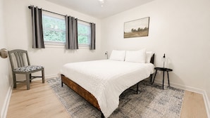 A bedroom with a bed, a chair, a bedside table, a ceiling fan, and a window with curtains.