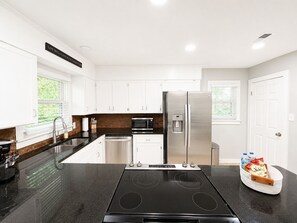 Une cuisine moderne avec des armoires blanches, un réfrigérateur en acier inoxydable, un four encastré et un coin café.