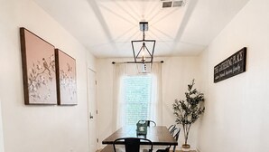 A dining area with a wooden table, black chairs, a pendant light, and a sign on the wall.