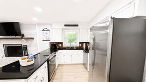 A modern kitchen with white cabinets, a stainless steel refrigerator, a black countertop, and a fireplace.