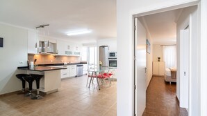 A modern kitchen with white cabinets, a central island, and bar stools. There is a dining area with a table and chairs. - GuestReady - Seaside Retreat (Funchal)
