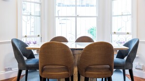 Un coin repas comprenant une table et quatre chaises, de grandes fenêtres agrémentées de barreaux en fer décoratifs et une vue sur l’extérieur.