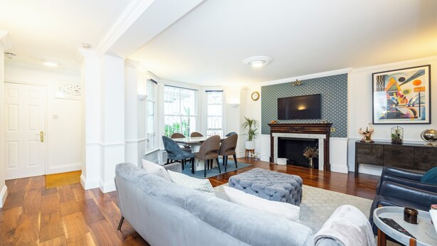 Un salon moderne avec un canapé gris, un coin repas avec des chaises, une cheminée et un téléviseur à écran plat fixé au mur.