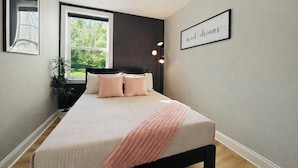 Un dormitorio con cama, lámparas de noche, una ventana y un cartel en la pared.