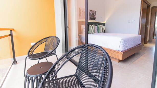 A bedroom with a bed, a sliding glass door, and two wicker chairs. - PF Hotel (Puerto Plata)