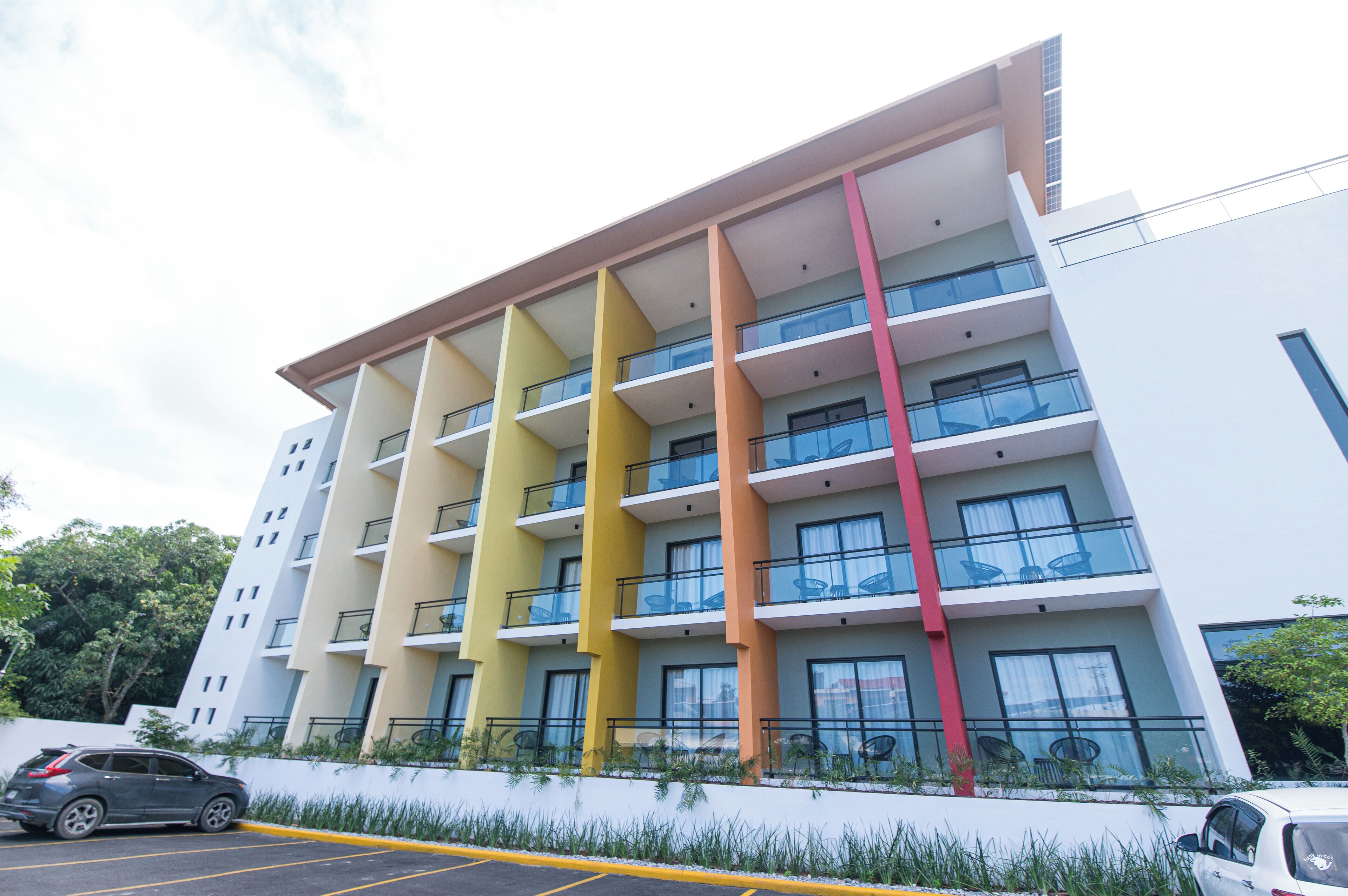 A multi-story hotel with balconies and a parking area in front.