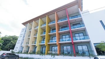 A multi-story hotel with balconies and a parking area in front.