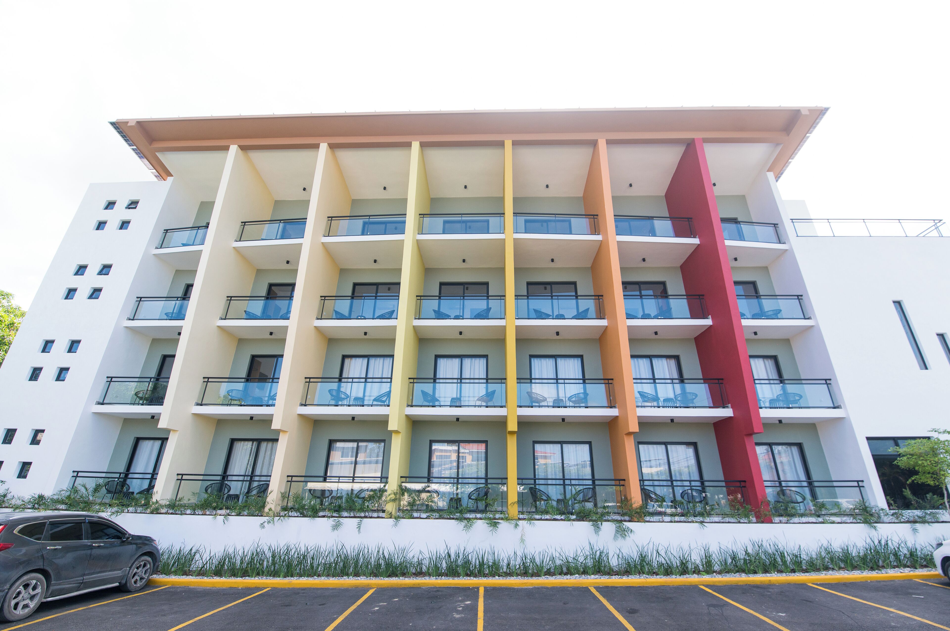 A multi-story hotel with balconies, a parking lot, and a modern architectural design.