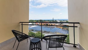 A balcony with two black chairs and a small table, overlooking a cityscape with buildings and solar panels. - PF Hotel (Puerto Plata)