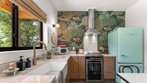 Una cocina moderna con un amplio ventanal, una campana extractora de acero inoxidable, un refrigerador verde azulado antiguo y un microondas.