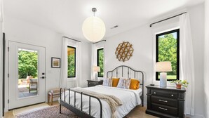 Un dormitorio con cama, mesitas de noche, una lámpara colgante y vistas al verde exterior.