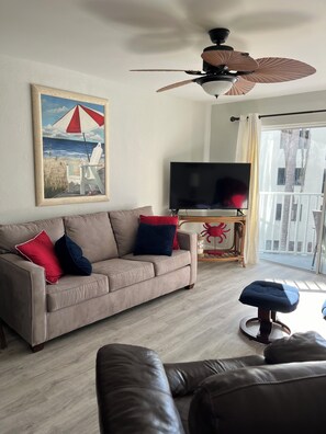 A living room with a beige sofa, a television, a ceiling fan, and a painting of a beach scene. - Romantic Beach Front Retreat with Spectacular Sunsets  just steps to the Beach! (Fort Myers Beach)