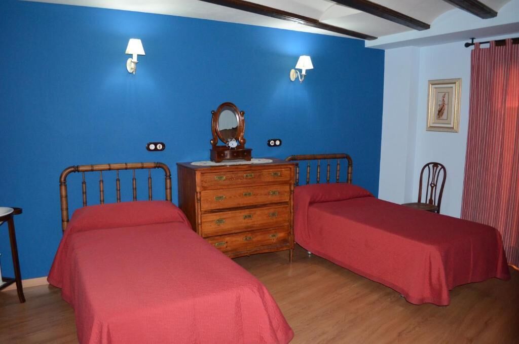 Ein Zimmer mit zwei Einzelbetten, einem Holzschrank mit Spiegel, zwei Wandlampen und einem gerahmten Bild an der Wand.