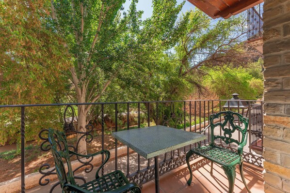 A balcony with a table and two chairs, surrounded by trees and a stone wall.